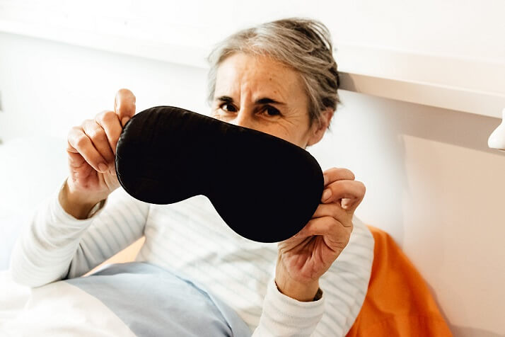 holding up a black sleep mask in bed